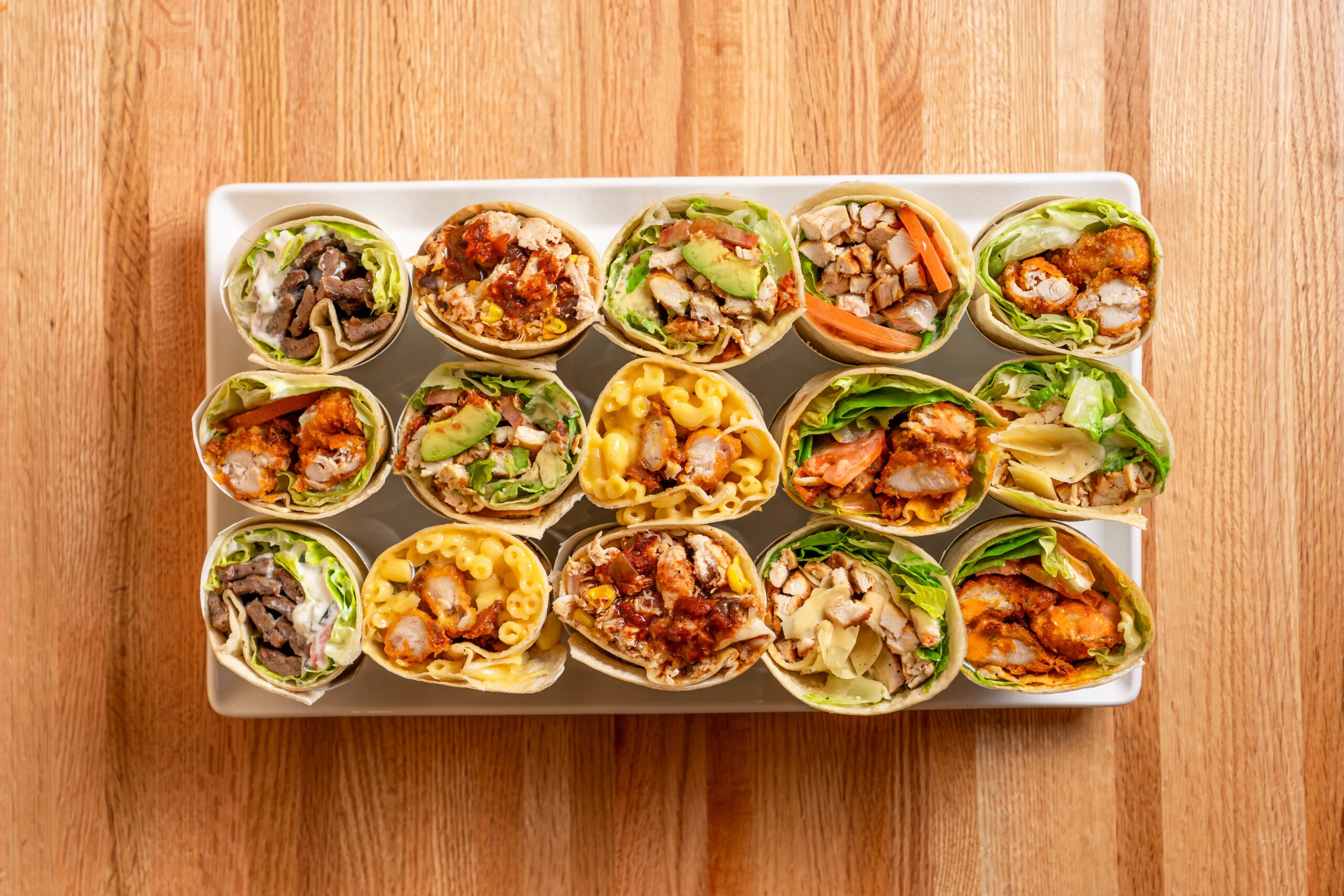 Assorted bite sized appetizers topped with colorful vegetables and herbs on a rectangular wooden platter.